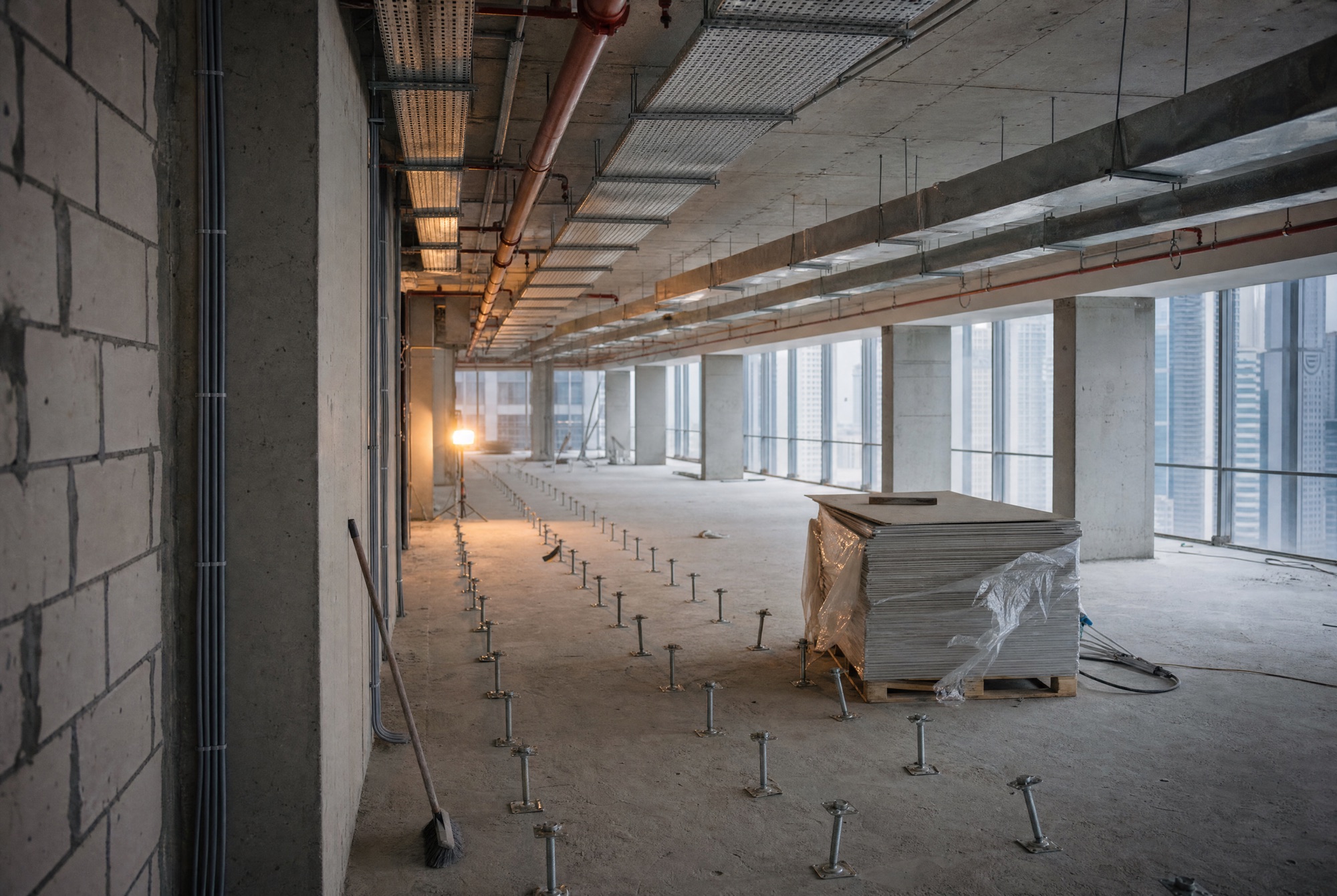 The same floor at first fix – ducting and cable trays in parallel lines under the soffit, rows of raised-floor pedestals set out below