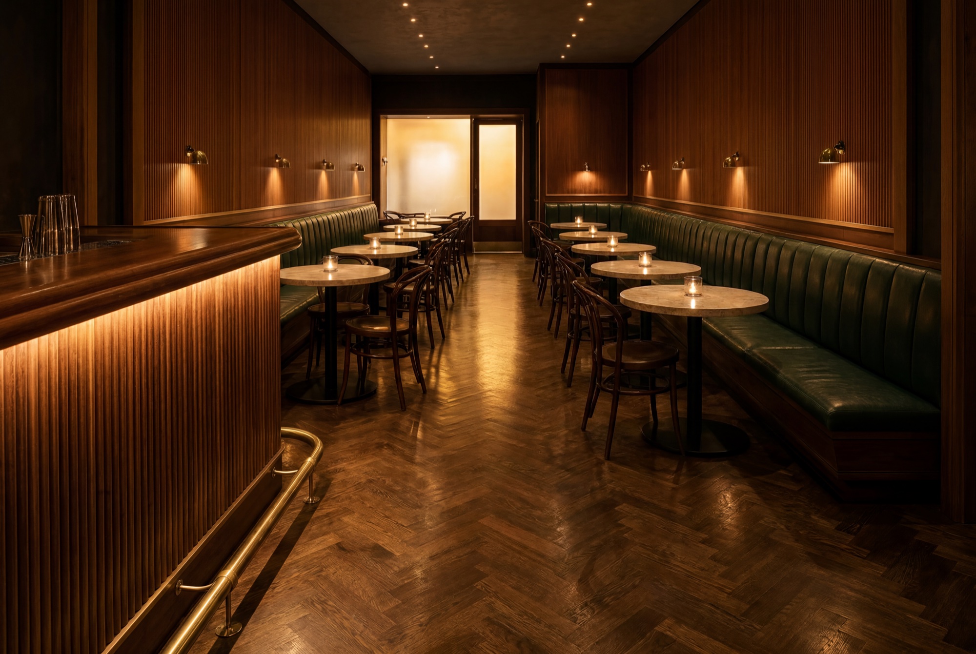 The finished dining room seen from beside the bar – green leather banquettes, candles lit, the entrance glowing at the far end
