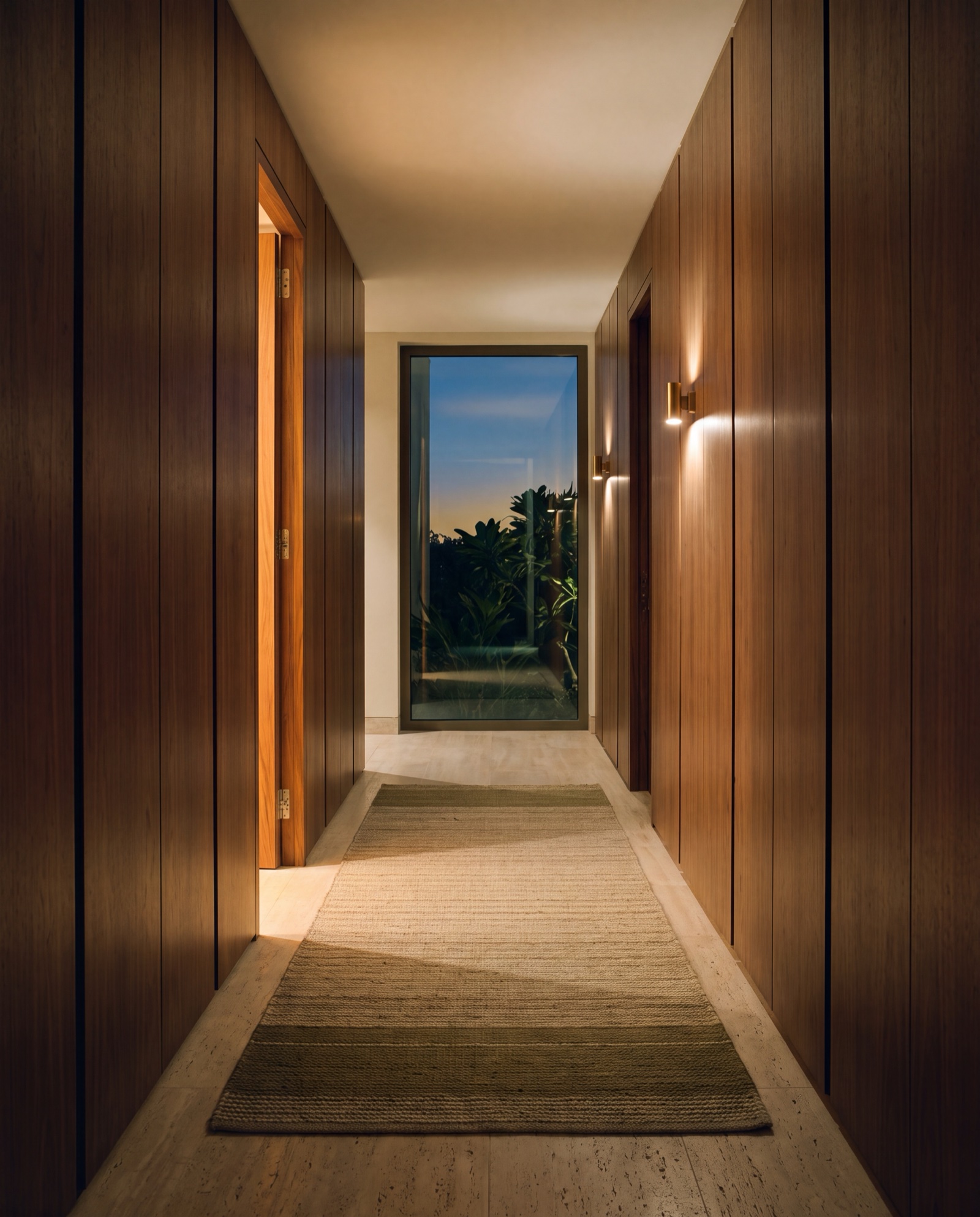 A corridor of flush walnut doors at dusk, one door ajar